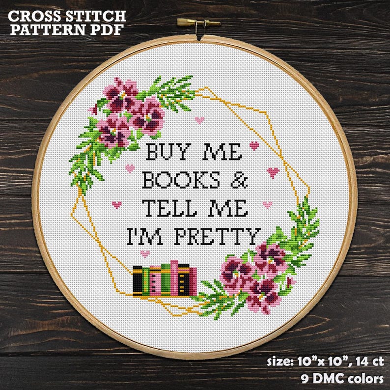 Cross-stitch pattern in a wooden hoop. The design features the text "BUY ME BOOKS & TELL ME I'M PRETTY" surrounded by floral and geometric elements. The finished size is 10" x 10".