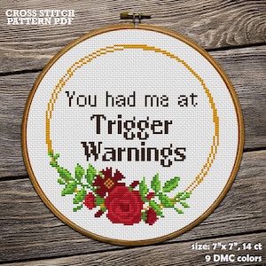May include: Cross stitch pattern PDF for a 7 inch by 7 inch hoop. The pattern features a floral wreath with red flowers and green leaves surrounding the text "You had me at Trigger Warnings".