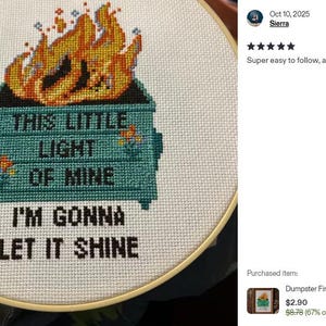 Cross-stitch embroidery in a wooden hoop. The design features a teal dumpster with flames and the text "THIS LITTLE LIGHT OF MINE I'M GONNA LET IT SHINE" in black. The flames are orange and yellow.