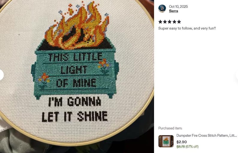 Cross-stitch embroidery in a wooden hoop. The design features a teal dumpster with flames and the text "THIS LITTLE LIGHT OF MINE I'M GONNA LET IT SHINE" in black. The flames are orange and yellow.