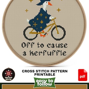 Puede incluir: Patr&oacute;n de punto de cruz con un ganso con sombrero y capa de mago en bicicleta, con el texto "Off to cause a kerfuffle". El dise&ntilde;o est&aacute; en un bastidor de bordado de madera. El tama&ntilde;o es de 14 x 19 cm.