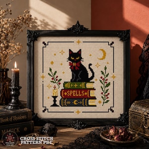 May include: A framed cross stitch pattern featuring a black cat with a red bow sitting on a stack of three books. The middle book is red with the word SPELLS in white text. The design includes green sprigs, yellow stars, and a crescent moon.