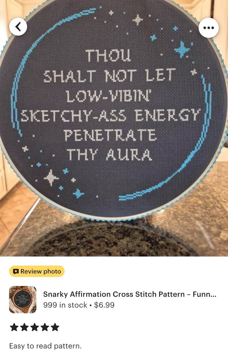 May include: A circular cross-stitch embroidery piece featuring a dark gray fabric background with white text that reads: THOU SHALT NOT LET LOW-VIBIN' SKETCHY-ASS ENERGY PENETRATE THY AURA. The design includes light blue stitched stars and a curved border.