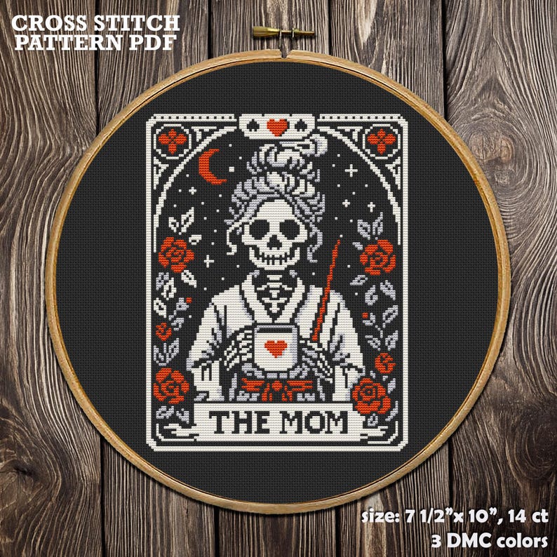 Cross-stitch pattern PDF featuring a skeletal figure holding a mug with a heart, surrounded by roses and stars. The design is framed in a wooden hoop, with the text "THE MOM" at the bottom. The pattern measures 7.5" x 10".