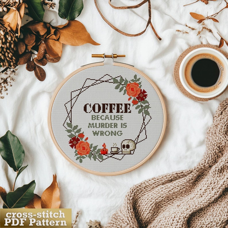 Cross-stitch pattern PDF featuring a skull holding a cup of coffee with the text "Coffee because murder is wrong". The pattern is surrounded by a floral wreath with red and orange flowers.