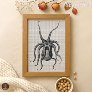 May include: A framed cross-stitch pattern featuring a detailed black and white octopus design. The artwork is displayed in a light brown wooden frame. The text "CROSS-STITCH PDF PATTERN" is visible in the upper right corner.