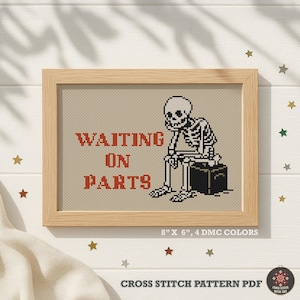 May include: A framed cross stitch pattern featuring a black and white skeleton sitting on a black box. The red text reads "WAITING ON PARTS". The design is set against a beige fabric background within a light wood frame, measuring 8 inches by 6 inches.