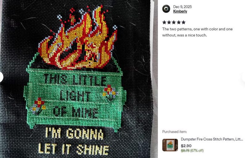 Cross-stitch design on black fabric featuring a green dumpster engulfed in flames. The text reads "THIS LITTLE LIGHT OF MINE, I'M GONNA LET IT SHINE" in yellow and green. The flames are red, orange, and yellow.