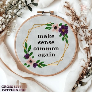 以下が含まれることがあります： 木製のフレームに入ったクロスステッチのデザインで、黒い文字で「make sense common again」と書かれています。デザインには、金色の幾何学的なフレームと、ピンク、紫、緑の花柄のアクセントが含まれています。「Cross Stitch Pattern PDF」の文字が下にあります。