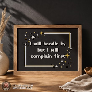 Può includere: Un motivo a punto croce incorniciato su sfondo nero con testo bianco che recita: I will handle it, but I will complain first. Il design presenta un bordo rettangolare dorato e bianco con piccoli accenti a forma di stella bianchi e oro.