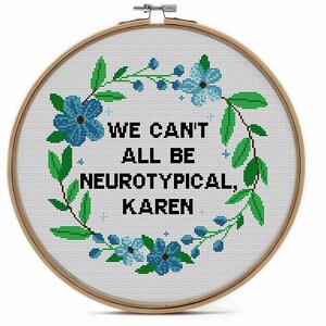 May include: A cross-stitch embroidery hoop with the text "WE CAN'T ALL BE NEUROTYPICAL, KAREN". The design features a floral wreath with blue flowers and green leaves. The hoop is made of wood.