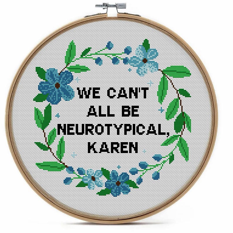 May include: A cross-stitch embroidery hoop with the text "WE CAN'T ALL BE NEUROTYPICAL, KAREN". The design features a floral wreath with blue flowers and green leaves. The hoop is made of wood.