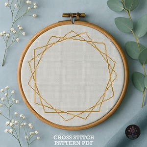 May include: A circular wooden embroidery hoop containing white Aida fabric with a geometric cross stitch pattern in gold thread. The design features overlapping angular lines forming a star-like shape. The text CROSS STITCH PATTERN PDF is visible.