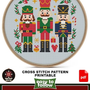 May include: A cross-stitch pattern featuring three toy soldiers in red, green, and blue uniforms, set against a light blue background. The design is framed in a wooden hoop and includes Christmas-themed elements. The text "CROSS STITCH PATTERN PRINTABLE" is also visible.