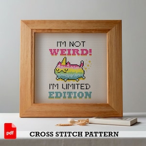 Peut inclure: Un modèle de point de croix représentant un chat de dessin animé avec une corne de licorne. Le chat est arc-en-ciel et a un nez rose. Le texte dit "Je ne suis pas bizarre ! Je suis une édition limitée".