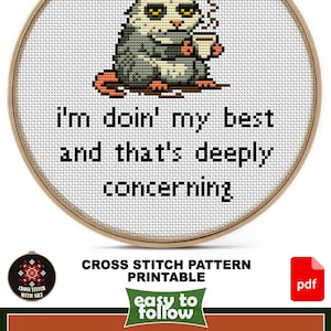 May include: Cross-stitch pattern featuring a possum holding a mug, stitched on white fabric within a wooden hoop. The text reads "I'm doin' my best and that's deeply concerning." The design size is 5 1/2" x 5 1/2".