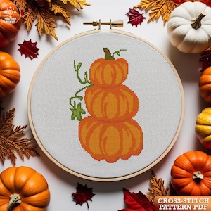 May include: A cross-stitch pattern of stacked orange pumpkins with green vines, set in a wooden embroidery hoop. The image is surrounded by pumpkins, fall leaves, and the text "CROSS-STITCH PATTERN PDF".