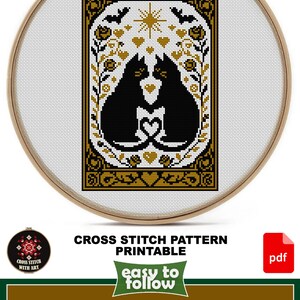 May include: Cross-stitch pattern featuring two black cats with a heart-shaped design, framed in a wooden hoop. The design includes the text "THE LOVERS" and is labeled "CROSS STITCH PATTERN PRINTABLE". The design size is 6 1/2" x 10".