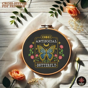 May include: A black and gold embroidery hoop with a cross-stitch design of a butterfly with the text "Antisocial Butterfly".