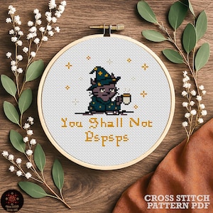 Pode incluir: Um bastidor de bordado em ponto cruz com um design de mago segurando uma caneca, com o texto "You Shall Not Dspsps" em dourado. O design está sobre um fundo branco, dentro de um aro de madeira.