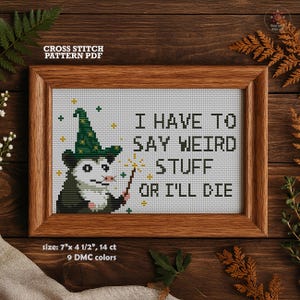 Puede incluir: Patrón de punto de cruz PDF en un marco de madera. El diseño presenta un opossum mago con una varita y el texto "I HAVE TO SAY WEIRD STUFF OR I'LL DIE." El tamaño del patrón es de 17,78 cm x 11,43 cm y utiliza 9 colores DMC.