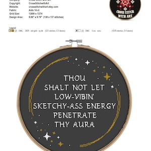 May include: A circular wooden embroidery hoop containing black fabric with white cross-stitched text that reads: THOU SHALT NOT LET LOW-VIBIN' SKETCHY-ASS ENERGY PENETRATE THY AURA. The design includes a curved gold line and small white and gold stars.