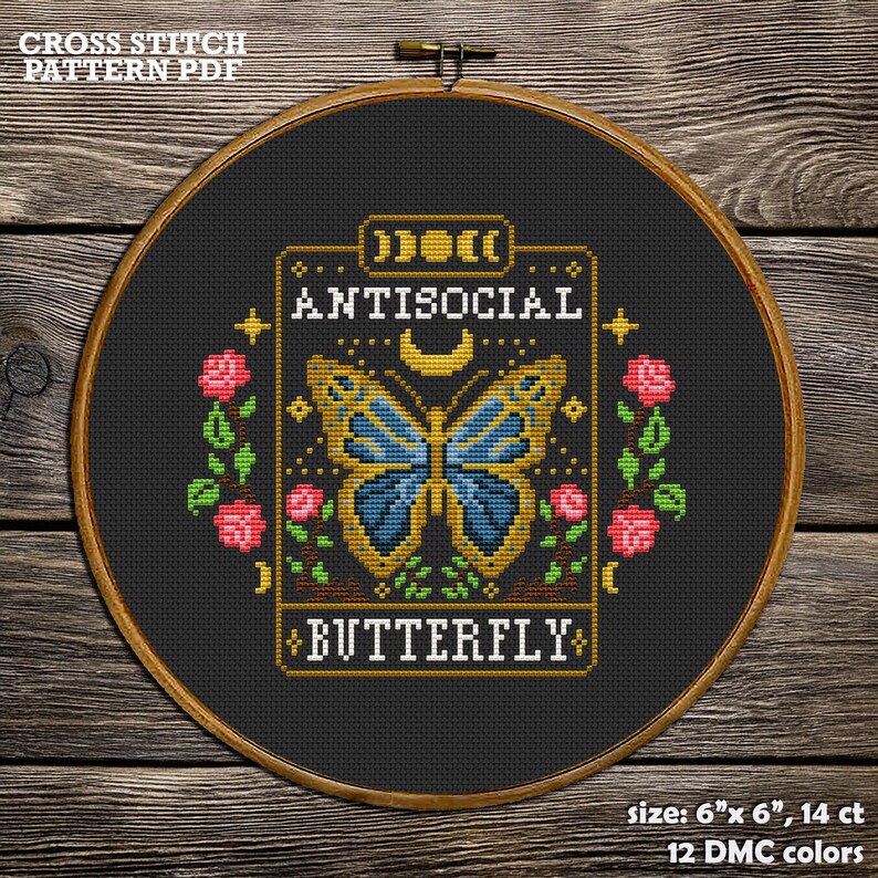 May include: A cross stitch pattern featuring a butterfly with blue wings and the text "ANTISOCIAL BUTTERFLY". The pattern is framed in a gold-colored border with a crescent moon and stars. The background is black and the pattern is 6 inches by 6 inches.