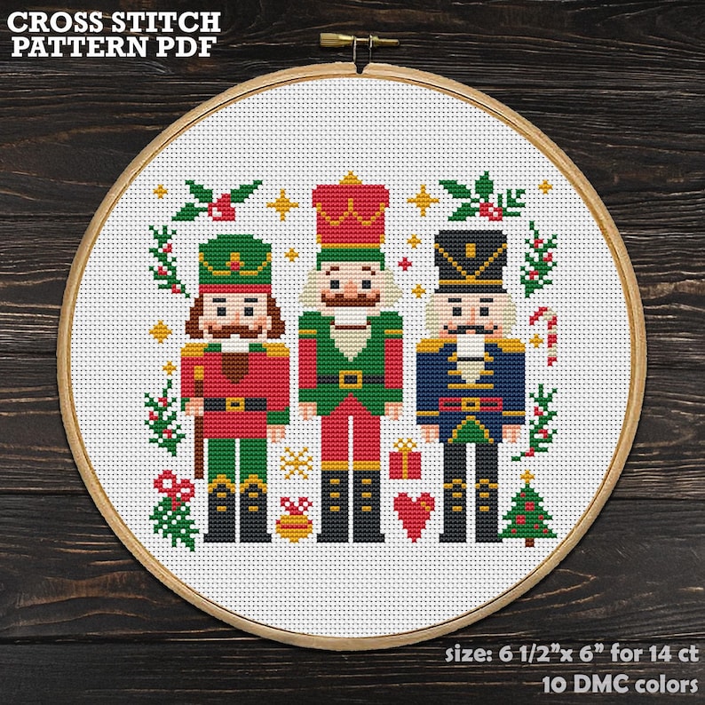 May include: A cross-stitch pattern featuring three toy soldiers in festive colors, set within a wooden embroidery hoop. The design includes Christmas elements like a tree, candy cane, and holly. The text "CROSS STITCH PATTERN PDF" is at the top. The size is 6.5" x 6" for 14 ct.