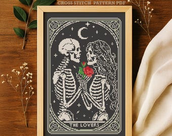 Peut inclure: Motif de point de croix encadré représentant deux squelettes tenant une rose rouge, sous un croissant de lune et des étoiles. Le texte "THE LOVERS" est en bas. Le cadre est en bois clair et le fond est gris foncé. Le texte "CROSS STITCH PATTERN PDF" est en haut.