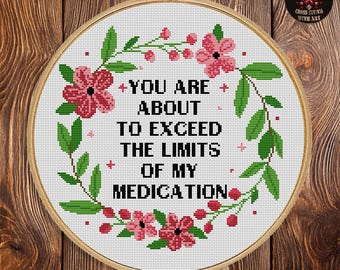 Puede incluir: Un patrón de punto de cruz en un bastidor de madera. El diseño presenta el texto "YOU ARE ABOUT TO EXCEED THE LIMITS OF MY MEDICATION" rodeado por una corona floral. El patrón mide 25,4 cm x 25,4 cm y utiliza 7 colores DMC.