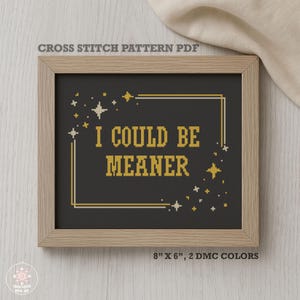 Könnte beinhalten: Ein gerahmtes Kreuzstichmuster mit dem Text "I COULD BE MEANER" in Gold auf schwarzem Hintergrund. Der Rahmen ist hellbraun und das Muster enthält Stern- und Quadratakzente. Die Maße sind 20 cm x 15 cm.