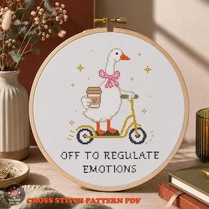 Puede incluir: Un bastidor de bordado circular de madera con un patrón de punto de cruz de un ganso blanco con pico y patas naranjas, con un lazo rosa, montado en un patinete amarillo mientras sostiene un café. El texto dice OFF TO REGULATE EMOTIONS.