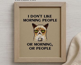 May include: A framed cross-stitch pattern with the text "I DON'T LIKE MORNING PEOPLE OR MORNING, OR PEOPLE" and a grumpy cat design. The frame is light brown, and the pattern is 5" x 7". The design uses 8 DMC colors.