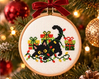 May include: A circular wooden embroidery hoop containing a cross-stitch design of a black cat tangled in multicolored Christmas lights and surrounded by wrapped gift boxes, finished with a dark red velvet ribbon tied at the top for hanging.