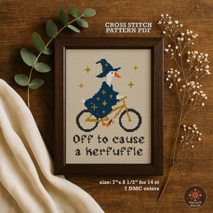 Könnte beinhalten: Gerahmtes Kreuzstichmuster-PDF in einem dunklen Holzrahmen. Der Kreuzstich zeigt eine Gans mit Zaubererhut und -robe, die Fahrrad fährt. Der Text "Off to cause a kerfuffle" steht darunter. Die Rahmengröße beträgt 17,78 cm x 21,59 cm.