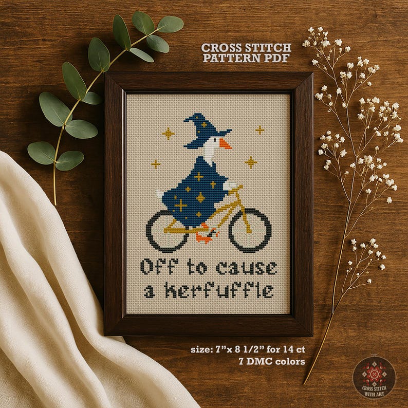 Cross stitch pattern PDF framed in a dark wood frame. The cross stitch depicts a goose wearing a wizard hat and robe, riding a bicycle. The text "Off to cause a kerfuffle" is below the goose. The frame size is 7" x 8 1/2".