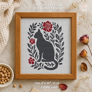 Könnte beinhalten: Kreuzstichmuster mit einer schwarzen Katze, die in einem Kranz aus roten Blumen und Blättern sitzt. Das Muster ist 20,3 cm x 25,4 cm groß und verwendet 14er Aida-Stoff. Es benötigt 2 DMC-Farben.