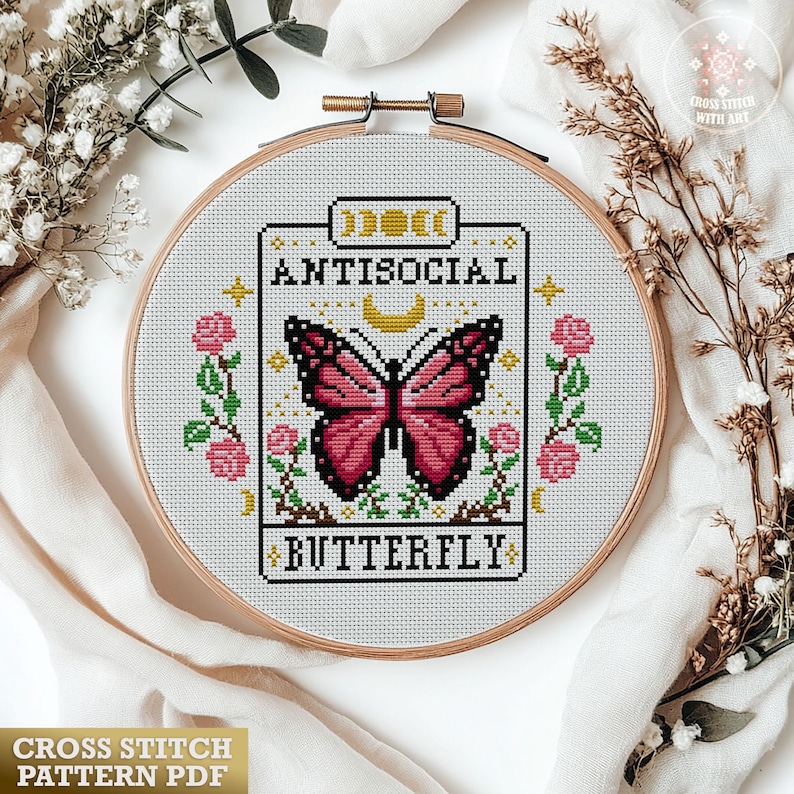K&ouml;nnte beinhalten: Ein Kreuzstichmuster in einem Holzrahmen mit einem rosa Schmetterling und dem Schriftzug "Antisocial Butterfly". Das Design ist von rosa Rosen und Gr&uuml;n umgeben. Der Text "Cross Stitch Pattern PDF" befindet sich unten.