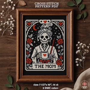May include: Framed cross-stitch pattern featuring a skeleton figure holding a mug with a heart, surrounded by roses and stars. The text "THE MOM" is displayed below the figure. The frame is 7.5" x 10" and the pattern uses 3 DMC colors.