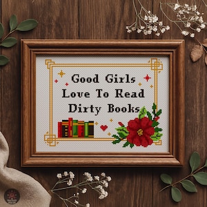 May include: Framed cross-stitch artwork with the text "Good Girls Love To Read Dirty Books." The design features a floral arrangement, books, and decorative elements within a wooden frame. The background is dark wood.