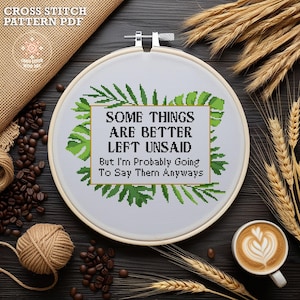 Op de afbeelding: Cross-stitch patroon PDF voor een witte borduurring met groene, weelderige bladeren rondom de tekst "Sommige dingen zijn beter onuitgesproken, maar ik ga ze waarschijnlijk toch zeggen."