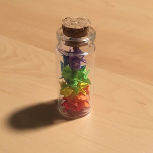 Tiny hand-folded origami cranes in a small jar