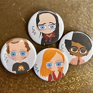 May include: Four round buttons with cartoon characters on them. Each button has the text "Firefly Flo" on it. The characters are a woman with black hair, a man with brown hair, a man with brown skin and black hair, and a woman with blonde hair.