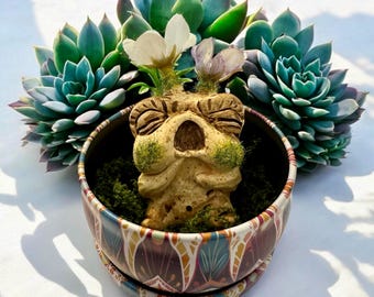 Babybeige en aardse Mandrake met witte en mauve bloemen, met de hand gesneden en beschilderd, in een metalen pot met groene mosvlokken