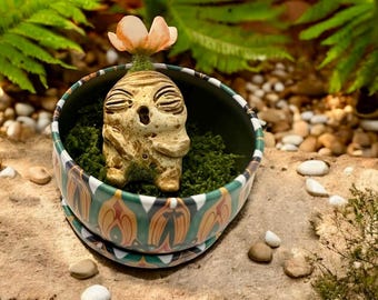 Beige en aardse baby Mandrake met oranje bloem, met de hand gesneden en beschilderd, in zijn metalen pot met groene mosvlokken