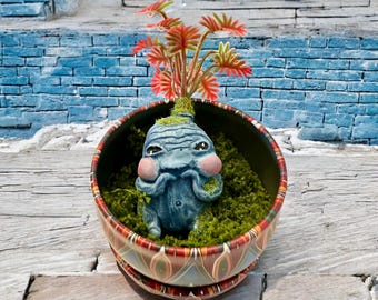 Babyblauw getinte Mandragora met rode plant, met de hand gesneden en beschilderd, in zijn metalen pot met groene mosvlokken