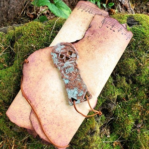 May include: A vintage-style scroll with music notes printed on it. The scroll is rolled up and tied with a brown leather cord. A turquoise blue skull charm is attached to the cord.