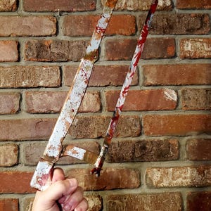 May include: A vintage hacksaw with a rusty, aged appearance and red splatters, held against a brick wall. The saw's blade and frame are stained, creating a horror or Halloween aesthetic.