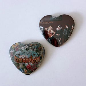 May include: Two heart-shaped buttons. One features a floral design with the text "WELCOME TO THE SOUND" and "PRETTY ODD". The other button has a band image with the text "NIC! AT THE DISCO ER YOU CAN'T SWEAT OUT".