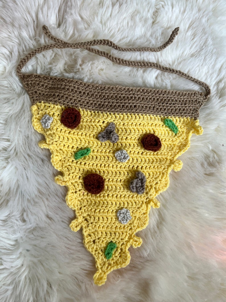 Puede incluir: Una rebanada de pizza de ganchillo con una corteza marr&oacute;n, queso amarillo, pimientos verdes y pepperoni marr&oacute;n y gris.